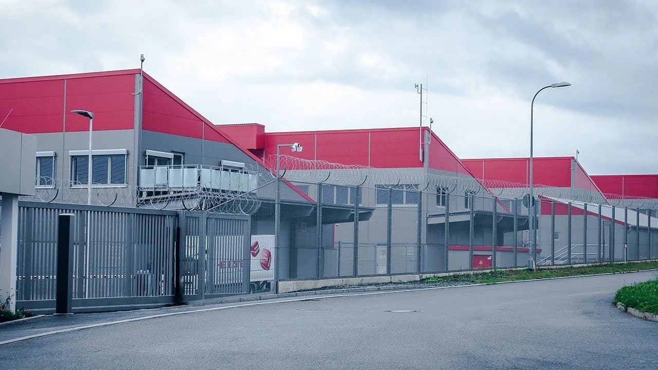 Außenansicht des rot-grauen Hetzner-Rechenzentrums mit umzäuntem Gelände